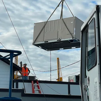 A crane lifting a new rooftop HVAC unit on a Modern Air Services commercial job